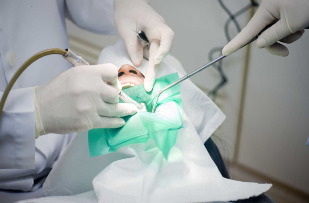 A close up of a dentists hands holding dental tools while performing a procedure on a patient with their mouth open