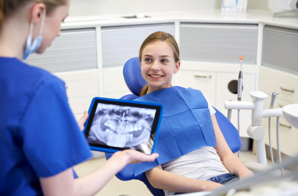 A female dentist explaining a dental procedure to a child while holding a dental X-ray image.