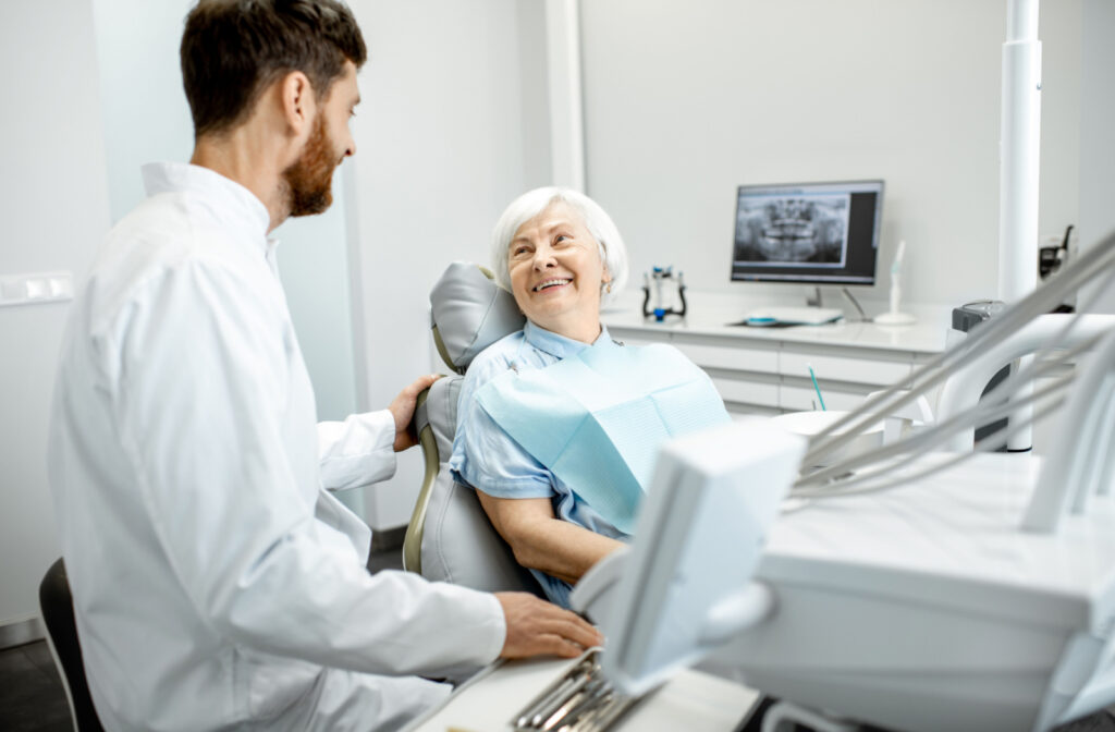 A senior woman sitting in a dental chair and smiling at her male dentist.
