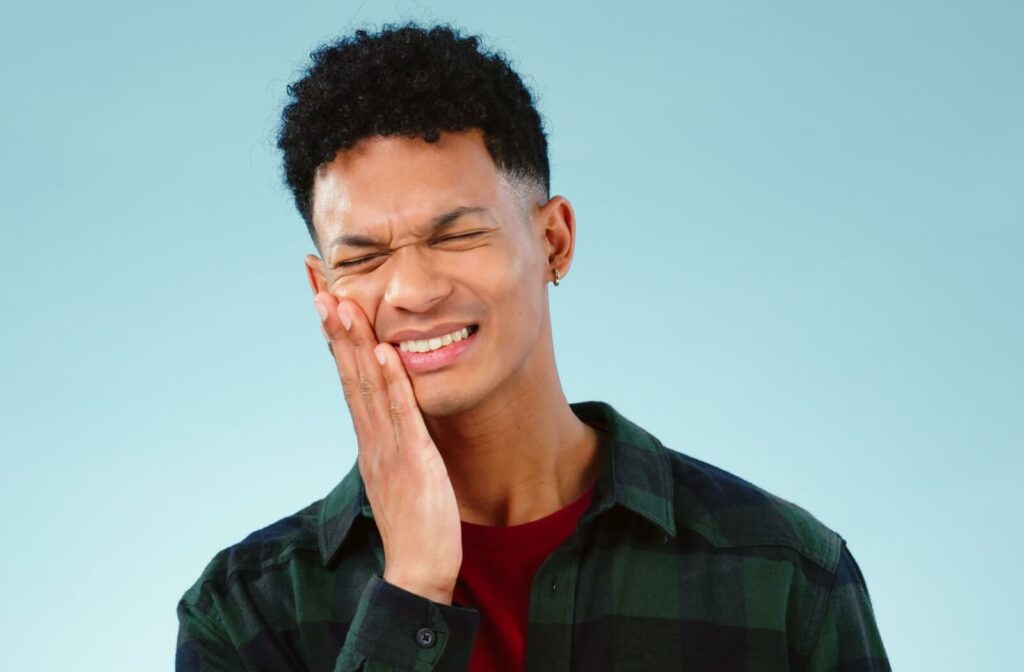 A person stands against a blue background and holds the right side of their jaw in pain