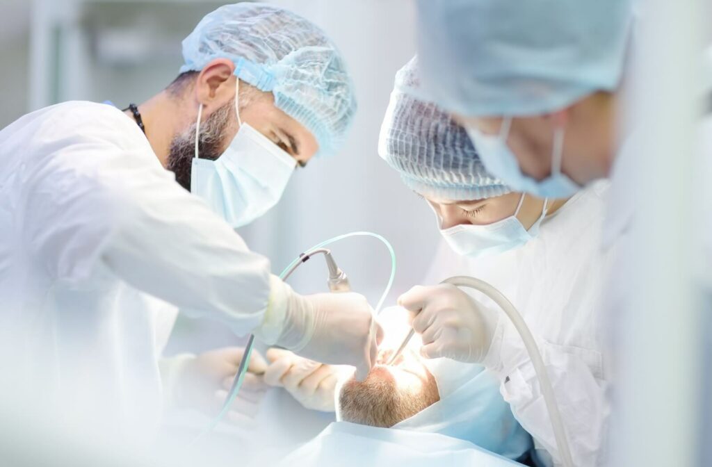 A person undergoing dental surgery with 3 dental surgeons in scrubs and blue caps working on them.