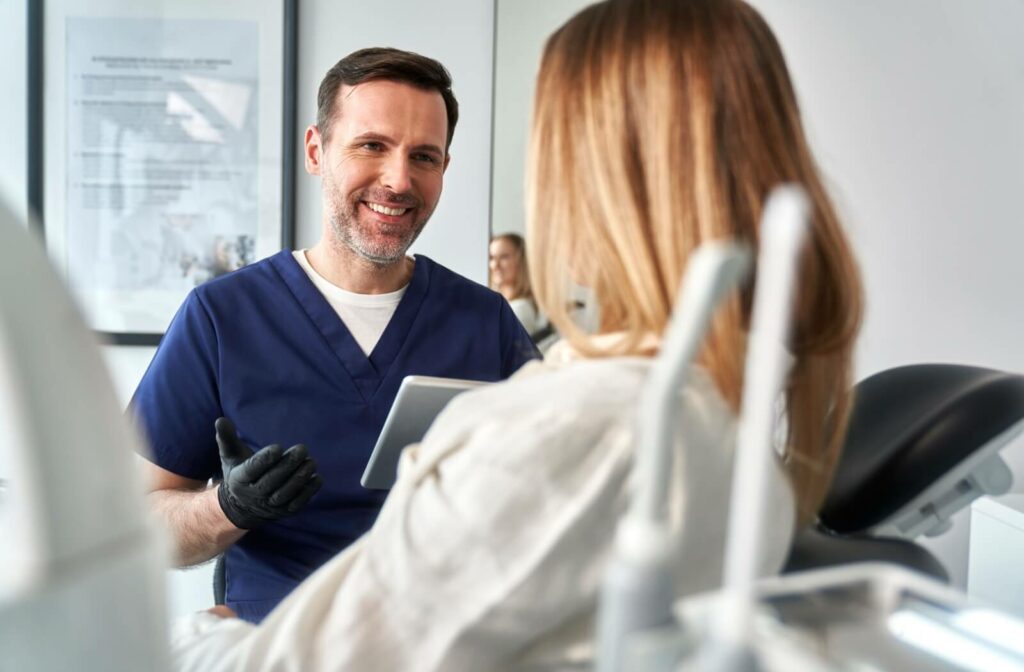 A dental patient sitting in the chair and looking away from the camera at her dentist as he smiles and explains a treatment.