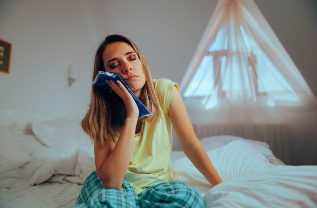 a patient at home applies a cold compress to their cheek to help reduce inflammation, wondering if previous dental work is causing TMJ.