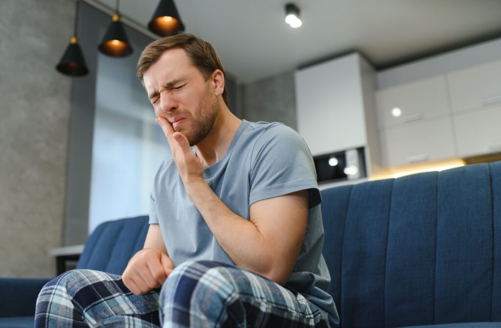 A young adult rubbing their jaw in discomfort on the couch at home due to wisdom tooth pain.